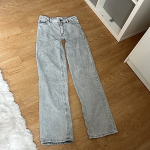 Gråa raka jeans från Lindex - Snygga gråa jeans från Lindex med rak passform och klassisk femficksdesign. Jeansen har en ljus tvätt och hög midja, perfekta för en avslappnad och trendig look. Tillverkade i jeansmaterial med dragkedja och knapp framtill.