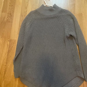 Grå stickad polotröja från Gina Tricot - Säljer en grå stickad polotröja från Gina Tricot. Tröjan har en hög ribbad krage och är långärmad med grovstickad struktur. Perfekt för kyliga dagar och enkel att styla med jeans eller kjol.