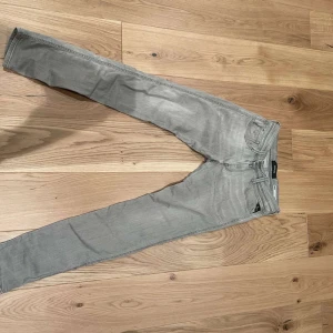 Grå jeans från Replay - Snygga grå jeans från Replay i modellen Anbass. De har en slim passform och är tillverkade i ett mjukt bomullsmaterial. Perfekta för en stilren look med klassiska femficksdetaljer och knappgylf.