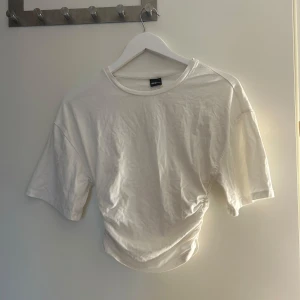 Vit t-shirt med snörning från Gina Tricot - Vit t-shirt från Gina Tricot med korta ärmar och cool snörningsdetalj i sidan som ger en tightande effekt. Använd fåtal gånger. 