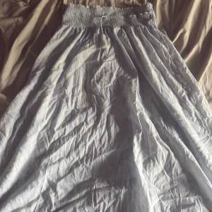 Ljusblå långkjol från Gina Tricot - Supersöt ljusblå långkjol från Gina Tricot med smockad midja och lätt, flowigt tyg. Kjolen har en enkel och stilren look som passar perfekt till sneakers eller sandaler. Den är luftig och har en mjuk känsla, perfekt för varmare dagar.