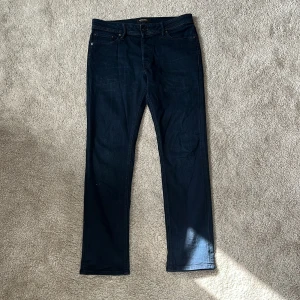 Mörkblå jeans från Jack & Jones - Snygga mörkblå jeans från Jack & Jones med klassisk femficksdesign och raka ben. Jeansen har normal passform och är tillverkade i ett mjukt denimtyg som sitter skönt hela dagen. Perfekta för dig som gillar stilrena och tidlösa jeans. Modellen är slim/straight i storleken 30/32