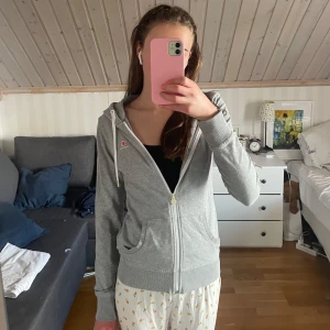 Grå hoodie från björnborg med dragkedja - Säljer en ljusgrå hoodie från Björn Borg med hel dragkedja framtill, huva med snörning och två fickor. Tröjan har ribbade muddar och en liten logga på bröstet. Perfekt för chill dagar eller när du vill vara extra bekväm.