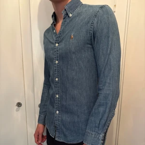 Blå jeansskjorta från Ralph Lauren - Säljer en klassisk blå jeansskjorta från Ralph Lauren med broderad logga på bröstet. Skjortan har lång ärm, knappar hela vägen och button-down krage. Perfekt till ett avslappnat men ändå stilrent uttryck. Skjortan har inte används mycket alls. (Jag på bilden är 190cm och väger 78kg