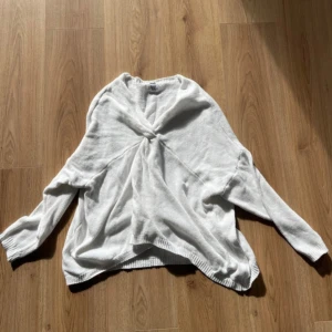 Vit stickad tröja med knut från Stajl - Vit stickad tröja från Stajl med snygg knutdetalj framtill. Tröjan har lång ärm, avslappnad passform och ribbade muddar. Perfekt för lager-på-lager och chill vibes.