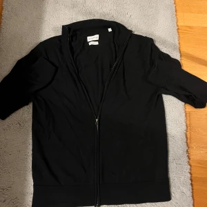 Mörkblå merinoulls full zip - Mörkblå stilren kofta i merinoull från These Glory Days, modell T Bertil Zip Cardigan. Koftan har hel dragkedja framtill, ribbade muddar och klassisk passform. Perfekt för lager-på-lager och stilren look. Vid frågor så är det bara att ställa! Säljer på grund av att den inte kommer till användande längre! Koftan passar dock mer som en M på grund av tvätt osv. För de som föredrar slim fit!