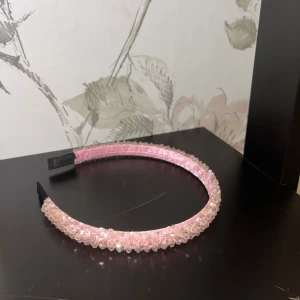 Rosa diadem med pärlor - Snyggt rosa diadem dekorerat med glittriga pärlor som ger en extra touch till din look. Diademet har en mjuk satinliknande yta och pärlorna är transparenta med rosa ton. Perfekt för att lyfta din frisyr och ge lite glam.