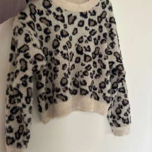 Leopardmönstrad fluffig tröja - Supermjuk och fluffig tröja med leopardmönster i beige, svart och bruna toner. Tröjan har rund halsringning och långa ärmar, perfekt för dig som vill sticka ut med en cool och trendig look.