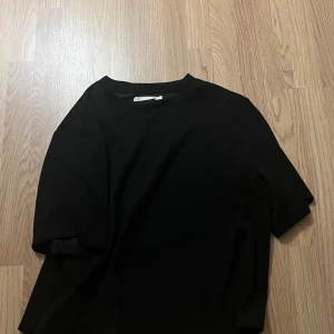 Svart basic t-shirt - En stilren svart t-shirt med klassisk rund hals och korta ärmar. Perfekt för dig som gillar en clean och enkel look. T-shirten har en rak passform och är gjord i mjukt material som känns skönt mot huden.