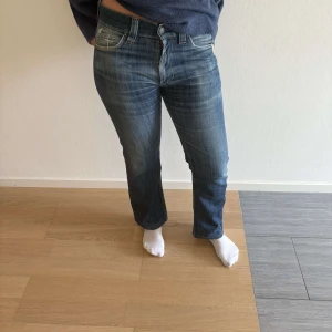 Levis 527 bootcut jeans blå - Snygga Levis 527 jeans i klassisk blå tvätt med bootcut passform. Jeansen har fem fickor, tydliga slitningar och kontrastsömmar. De sitter midja till höft och har en lätt utsvängd benvidd. Perfekta för dig som gillar en avslappnad men ändå stilren look.