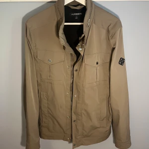 J.Lindeberg Bailey Jacka - Stilren och klassisk Bailey fieldjacka från J.Lindeberg i den sällsynta färgen walnut. Skicket är som nytt.