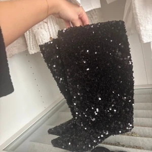 Svarta paljettstövlar med spetsig tå - Unika svarta stövlar täckta i glittrande paljetter, med spetsig tå och hög modell. Perfekta för dig som vill sticka ut🫶🏽 ena skon är lite sliten i tåspetsen på bild 3🥰 annars är som super fina och sköna att gå i. Klacken är låg ca 2 cm🥰