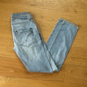 Dondup George Jeans - Säljer ett par ljusblå jeans från Dondup med slitningar och hål på benen för en cool, avslappnad look inga hål går rakt igenom modellen är Lucky men sitter som ett par dondup storleken är 33 men sitter mer åt 31-32 . Klassisk femficksmodell med raka ben och snygga detaljer. Perfekta för dig som gillar streetstyle och vill sticka ut lite extra.