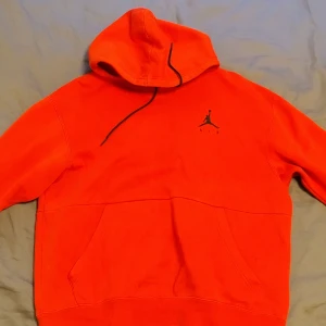 Röd hoodie från Jordan med logga - Säljer en röd hoodie från Jordan med klassisk Jumpman-logga på bröstet. Tröjan har huva med snörning och en stor magficka framtill. Perfekt för dig som gillar streetwear och sportig stil.