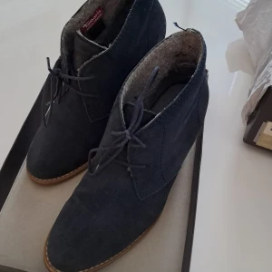 Mörkblå mockakängor från Tamaris - Snygga mörkblå kängor från Tamaris med snörning och rund tå. Utsidan är i mocka och insidan fodrad med mjuk polyester för extra komfort. Skorna har en låg klack och platt sula i gummi, perfekta för höst och vinter. Stilren design som passar till jeans och jacka.