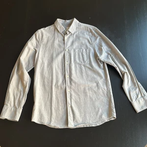 Grå skjorta från Filippa K, medium - Snygg grå skjorta från Filippa K i storlek medium. Klassisk modell med krage, bröstficka och vita knappar framtill. Tillverkad i mjuk bomull som känns skön mot huden. Perfekt för dig som gillar stilrena och enkla plagg. Nästan aldrig använd och i perfekt skick 