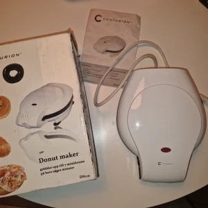 Donut Maker - Donut maker från Centurion, modell DN110. Bakar upp till 7 minidonuts åt gången på bara några minuter. Non-stick beläggning och temperaturindikator. 700W. Kommer med originalkartong, vilket är sliten men funkar ändå och en manual. Maskinen är i mycket gott skick.