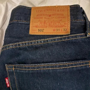 Levi's 501 mörkblå jeans W31 L32 - Klassiska Levi's 501 jeans i mörkblå denim med raka ben och snygga kontrastsömmar. Modellen har normal passform och ikonisk läderpatch bak i midjan. Perfekta för dig som gillar tidlös stil och vill ha ett par jeans som alltid funkar.