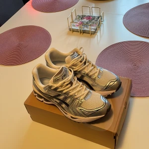 Asics Gel-Kayano 14 sneakers silver/vit - Säljer ett par Asics Gel-Kayano 14 sneakers i vit och silver med svarta detaljer. Skorna har mesh-överdel, syntetpaneler och snörning. Ikonisk retrodesign med rund tå och platt sula, perfekt för dig som gillar streetwear och coola detaljer.