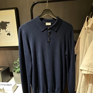 Marinblå pikétröja John Henric - Snygg marinblå pikétröja från John Henric med klassisk krage och tre knappar framtill. Tröjan är långärmad och har en slim passform som sitter riktigt bra. Materialet är merinoull, perfekt för dig som gillar stilrena och bekväma plagg. Använd ett fåtal gånger och i väldigt fint skick. Nypris 999kr.