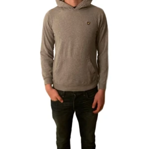 Lyle & Scott hoodie grå S - Snygg grå hoodie från Lyle & Scott med klassisk gul logga på bröstet. Tröjan har huva, magficka och långa ärmar. Perfekt för chill dagar och enkel att matcha.  Längd på tröjan: 62cm Bröstvidd: 49cm             Nypris: 650 kr. Mitt pris: 115kr
