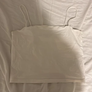 Vit linnetopp med smala axelband - Säljer en enkel och stilren vit linnetopp från Gina Tricot. Toppen har smala axelband och ärmlös design, perfekt för varma dagar. Materialet är mjukt och lätt, vilket gör den skön att bära. Passformen är normal och toppen är enfärgad utan detaljer.