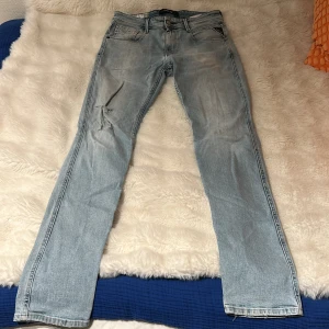 Replay Anbass ljusblå jeans herr - Säljer ett par Replay Anbass jeans i ljusblå tvätt med klassisk femficksdesign och snygga slitningar. Jeansen har raka ben och normal passform, med Replay-logga på fickan och läderpatch bak i midjan. Perfekta för en avslappnad och trendig look.