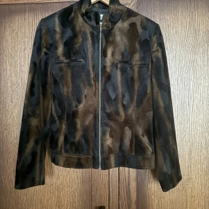 Brun och svart inne jacka från  Isolina Sartini - Snygg jacka  från Isolina Sartini i storlek 38. Jackan har ett brunt och svart mönster, raka linjer och dragkedja framtill. Den har två diskreta bröstfickor med dragkedja och en klassisk krage. Perfekt för dig som vill sticka ut med en unik look.