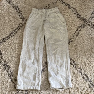 Ljusgrå mjukisbyxor med snörning - Ljusgrå mjukisbyxor med resår och snörning i midjan. Byxorna har raka ben, två fickor fram och en bakficka. Perfekta för chill dagar eller när du vill vara extra bekväm. Tillverkade i mjukt bomullsmaterial.