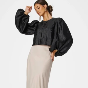 Svart blus med puffärmar från Bubbleroom - Säljer en svart blus från Bubbleroom med riktigt stora puffärmar och croppad passform. Blusen har rund halsringning och är tillverkad i ett glansigt syntetmaterial som ger en lyxig känsla. Perfekt för dig som vill sticka ut med volym och cool siluett.