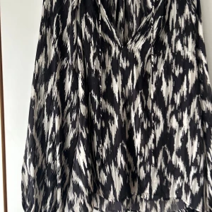 Svartvit omlottklänning från H&M - Säljer en svartvit omlottklänning från H&M med coolt abstrakt mönster. Klänningen har v-ringning, knytband i midjan och långa ärmar. Materialet är lätt och flowy, perfekt för dig som gillar statement-plagg med edge.