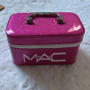Glittrig rosa sminkväska från MAC - Snygg och glittrig rosa sminkväska från MAC med vit dragkedja och metallhandtag. Väskan har ett spegelinslag på insidan och är perfekt för smink eller småprylar. Rektangulär form och coolt MAC-tryck på framsidan.