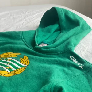 Grön Hammarby hoodie från Craft - Grön hoodie från Craft med Hammarby IF-logga på bröstet. Tröjan har huva, magficka och tryckt Craft-logga på axeln. Perfekt för dig som vill visa ditt stöd för Bajen. Mjuk och skön med klassisk passform. Frakt får betalas själv