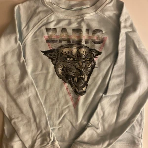 Ljusblå långärmad tröja Zadig & Voltaire - Cool ljusblå långärmad tröja från Zadig & Voltaire med paljettbroderad panter och texten ZADIG framtill. Tröjan har en avslappnad passform och är perfekt för dig som vill sticka ut med ett statement-plagg.BARN STORLEK ÅR 12!!!!!