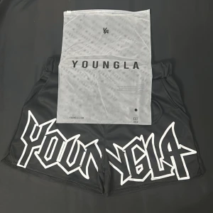 YoungLA svarta shorts - Grymma svarta shorts från YoungLA med stort vitt grafiskt tryck över hela framsidan. De har elastisk midja med snörning och är tillverkade i ett mjukt, syntetiskt material. Perfekta för dig som vill sticka ut med en streetstyle-look.