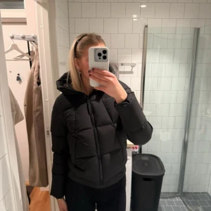 Svart pufferjacka Peak Performance - Säljer en svart pufferjacka från Peak Performance med huva och dragkedja. Jackan är vadderad och har en klassisk boxig passform, perfekt för kalla dagar. Snygg och enkel design som funkar till allt.