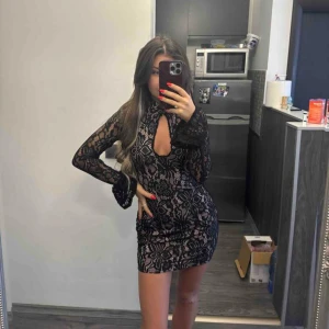 Svart spetsklänning med blommönster - Säljer en svart kort spetsklänning med blommigt mönster, klänningen har en öppning vid bröstet och snygg passform🥰