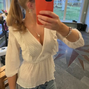 Vit omlottblus från ONLY - Säljer en jättefin vit omlottblus från ONLY!💕 Storlek XS. Blusen har ett ribbat mönster, volangdetaljer både fram och bak samt elastisk midja. Den har trekvartsärmar med lätt puff och v-ringad hals. Nästan aldrig använd, och säljer för att jag inte använder den!💕Tveka inte att höra av dig om du har frågor eller vill diskutera pris!