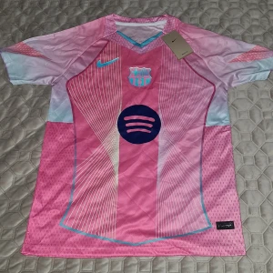 Barça x Nike rosa fotbollströja S - Barcelona fotbollströja från Nike i rosa och ljusblått med vita linjer och klubbmärke på bröstet. Tröjan har korta ärmar, Dri-FIT-material och Spotify-logga framtill. Snygg V-ringning med turkosa detaljer och modern design.