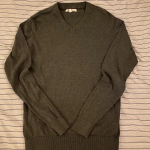 Mörkgrå v-ringad stickad tröja - Mörkgrå stickad tröja med v-ringad hals och långa ärmar. Tröjan har ribbade muddar vid ärmslut och nederkant, vilket ger en schysst och clean look. Perfekt för dig som gillar enkla och stilrena plagg i garderoben.
