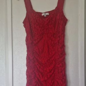 Röd spetsklänning med drapering - Supersnygg röd kort klänning från H&M med breda axelband och v-ringning. Klänningen är täckt av blommig spets och har draperade detaljer framtill som ger en cool och trendig look. Perfekt för dig som vill sticka ut med färg och mönster.