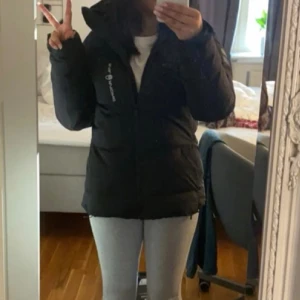 Svart dunjacka från Sail Racing M - Säljer en svart dunjacka från Sail Racing i storlek medium. Jackan har huva, dragkedja framtill och coola logodetaljer på bröstet och ärmen. Perfekt för kalla dagar med sin puffiga design och snygga look. Passar dig som gillar street och funktion.