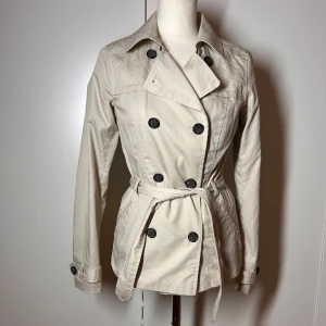 Kort beige trenchcoat only  - Trenchcoat  från only i storlek xs. Passar även s. Ganska tunn. Köp sker via köp nu, jag postar inom 24h. Kvar tills markerad såld 