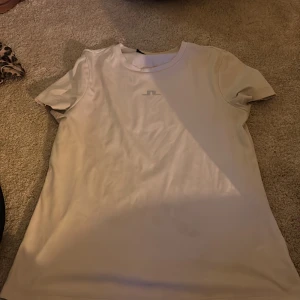 Vit t-shirt från J.Lindeberg - Snygg vit t-shirt från J.Lindeberg med diskret logga på bröstet. Klassisk rund halsringning och korta ärmar. Tillverkad i mjuk bomull som känns skön mot huden. Perfekt för en clean och stilren look. Köpt för 400 kr