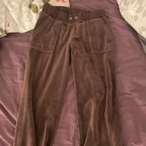 Bruna mjukisbyxor Juicy Couture S - Bruna mjukisbyxor från Juicy Couture i mjuk velour med bred resår i midjan. Stora fickor fram och bak med knappdetaljer. 