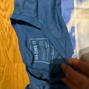 Blå t-shirt med tryck från IT:ONE11 - Säljer en blå t-shirt från IT:ONE11 i bomull. T-shirten har korta ärmar och ett stort färgglatt tryck framtill med motiv av en bil och strand. Perfekt för dig som gillar en chill och avslappnad stil.