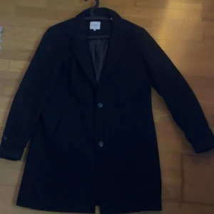 Jack&jones rock - Stilren svart rock från Jack & Jones i klassisk modell med knappar framtill och krage. Perfekt för dig som vill ha en clean och tidlös look. Fodrad insida och långa ärmar. Passar dig som gillar enkel och snygg stil.