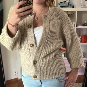 Beige stickad kofta från Zara - Supermysig beige stickad kofta från Zara med stora träknappar och ribbade detaljer. Koftan har kortare ärmar och är i bra skick.