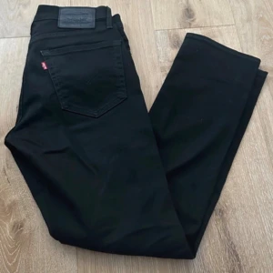 Svarta Levi's 511 jeans W30 L30 - Svarta Levi's Premium 511 jeans med klassisk femficksdesign och smal passform. Jeansen har svarta nitar, svart patch bak och är tillverkade i stretchig bomullsdenim för extra komfort. Perfekta för dig som gillar en clean och stilren look.