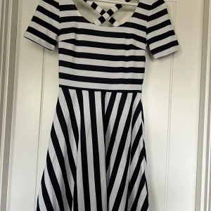 Randig kortklänning - Kortklänning som är vit/marin. Klänningen har rundad hals med korsade band i ryggen och korta ärmar. Aldrig använd.